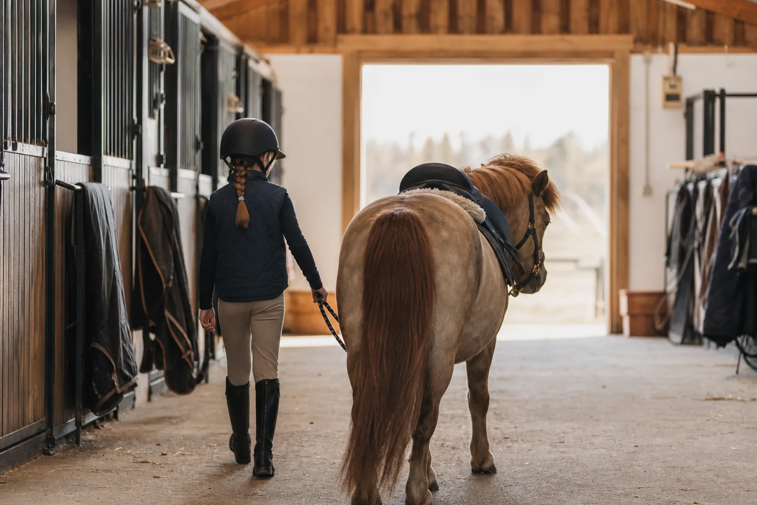 Barn i ridstövlar som leder en ponny i ett stall